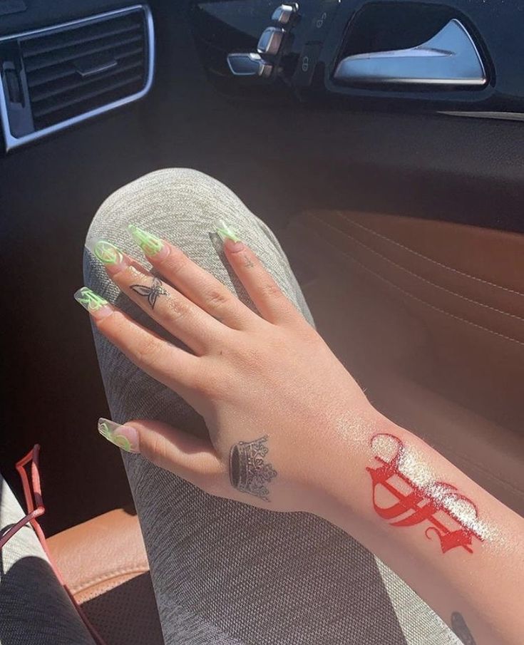 a woman's hand with green and white nail polish sitting in the drivers seat of a car