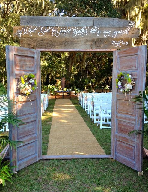 an outdoor ceremony setup with white chairs and wooden doors, decorated with flowers and greenery