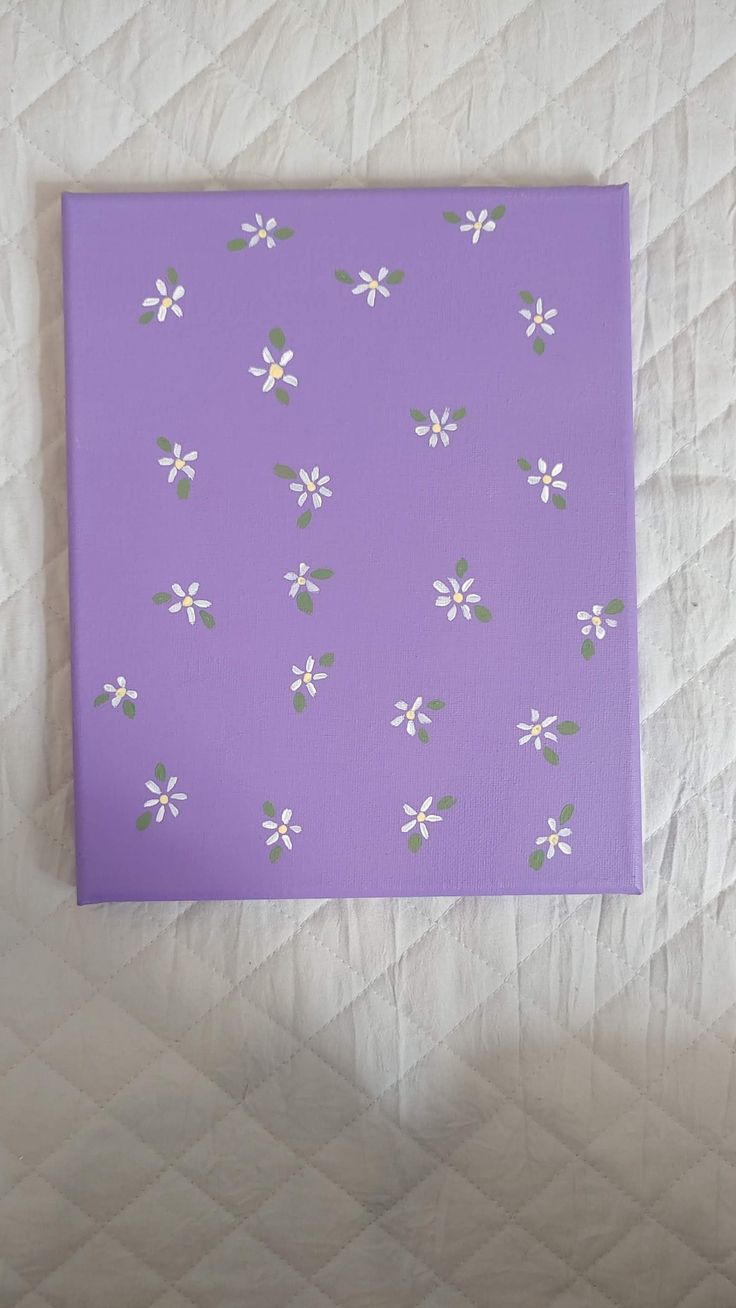 a purple canvas with white flowers on it sitting on top of a quilted surface