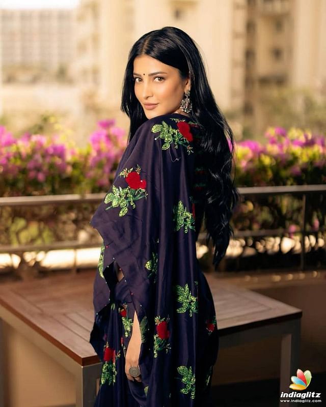 a woman wearing a blue dress with red flowers on it and long black hair standing in front of a wooden bench