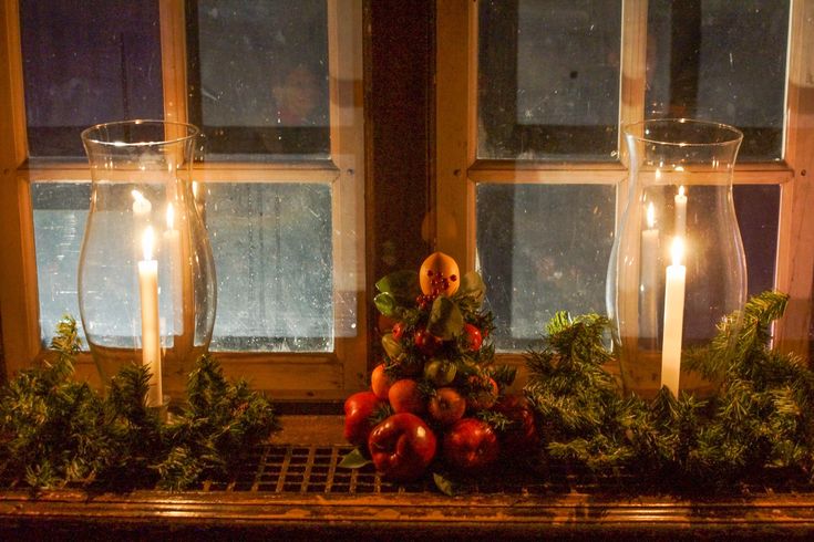 candles are lit on the window sill with fruit and greenery