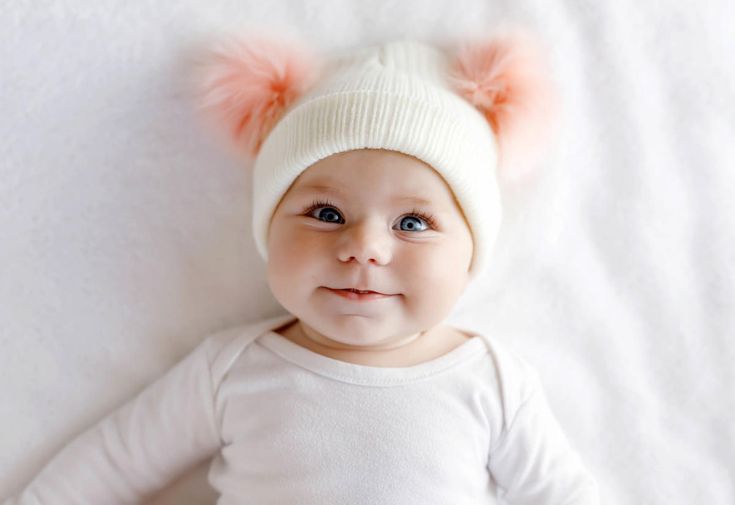 a baby wearing a white hat with orange pom poms on it's ears