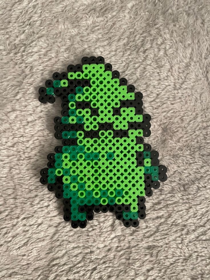 a green and black pixel art piece sitting on top of a white blanket