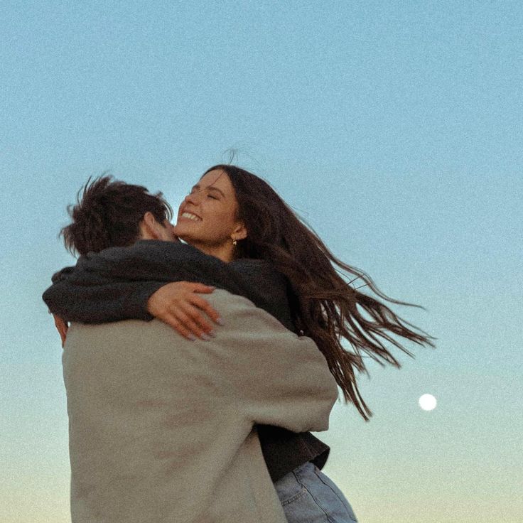 a man and woman hug each other as the moon is in the sky behind them