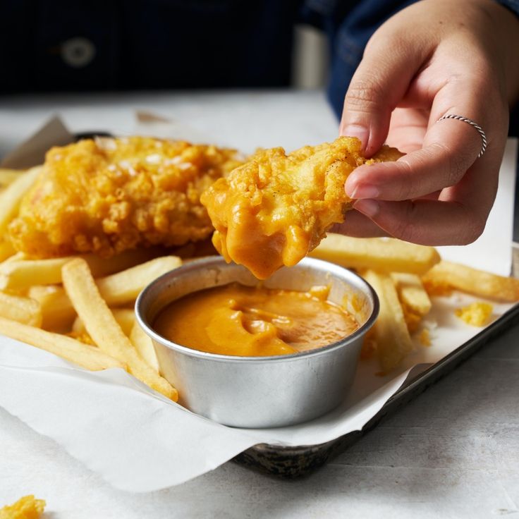 a person is dipping some food into a small bowl with sauce on it and fries in the foreground