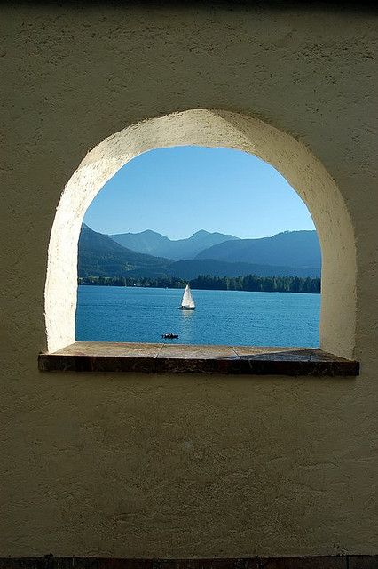 a window with a sailboat on the water in front of it and mountains in the background