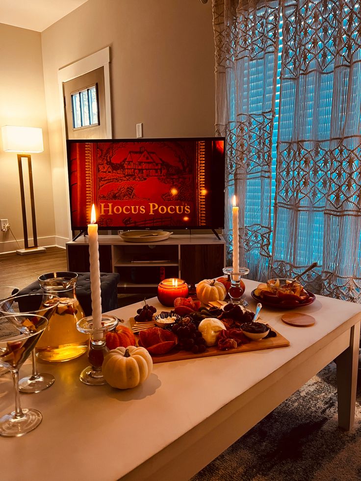 a table with candles and food on it in front of a television screen that says hoccus pocus