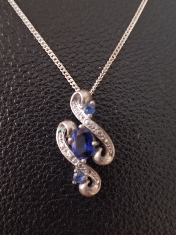 "Sterling silver pendant with blue stones stones and diamond chips. The pendant is a slide and has two s-type swirls. In the center is an oval blue stone and two small and two smaller stones are mounted on top and bottom of the blue stone. The blue stone is a lab created sapphire. Small diamond chips are mounted on the swirls. The slide is marked \"925\". It comes with a 16 inch sterling silver curb chain necklace." Blue Oval Pendant Necklace With Diamond Accents, Figaro Chain Necklace, Curb Chain Necklace, Dog Pendant, Silver Flats, Dry Brush, Blue Stones, Crafting Materials, Type S