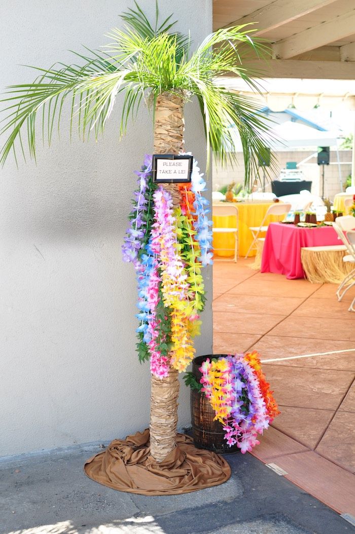 a palm tree decorated with leis and flowers on the side of a building next to a table