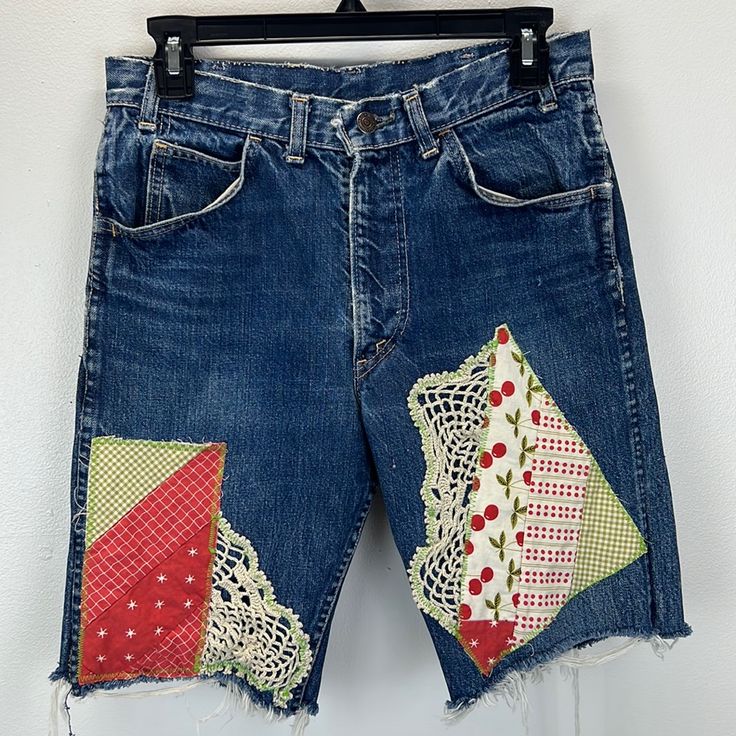 a pair of blue jean shorts with patchwork and lace on the side, hanging up against a white wall