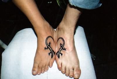 two people with tattoos on their feet sitting in front of a laptop computer and holding hands together