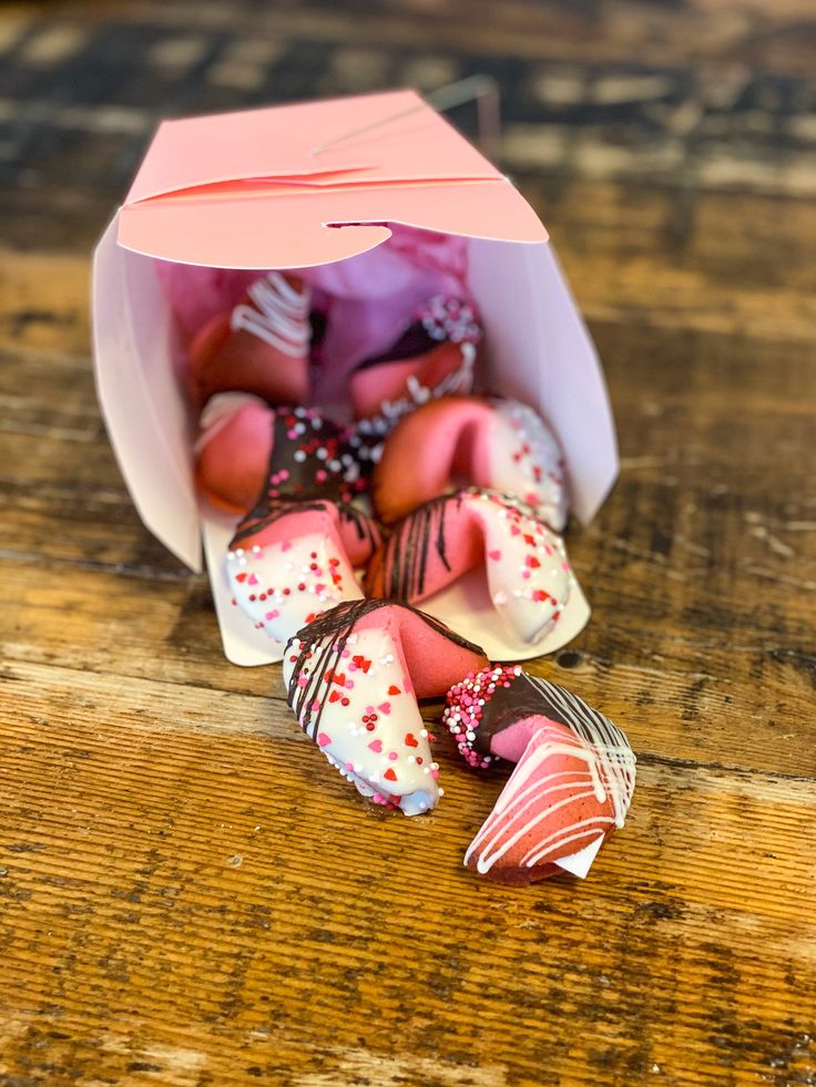 a pink box filled with chocolate covered donuts on top of a wooden table next to a paper bag