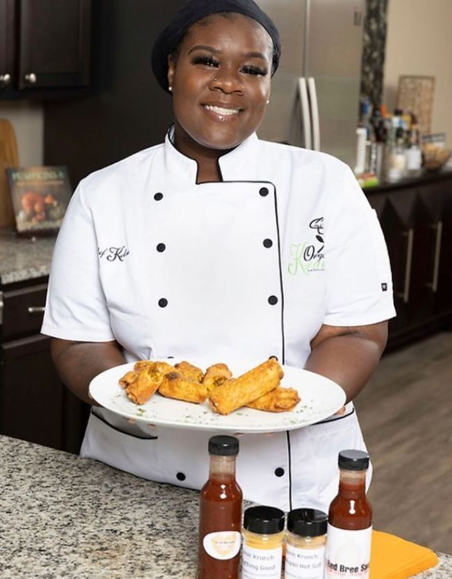 a woman in a chef's uniform holding a plate of food with sauces on it