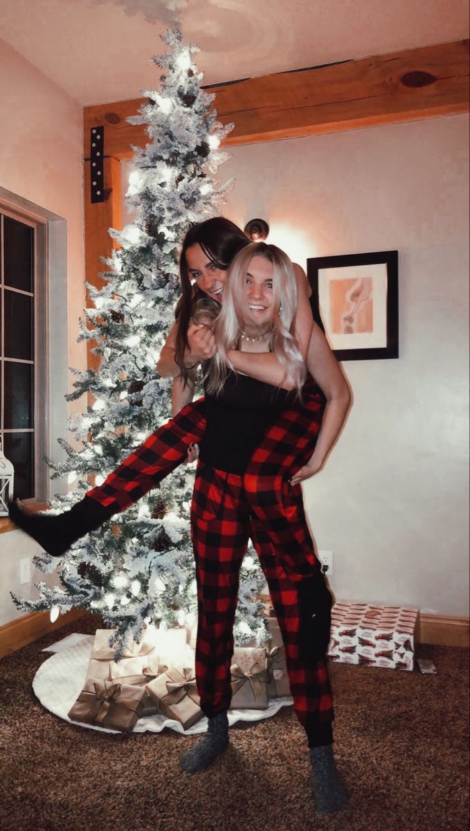 two women standing in front of a christmas tree with their arms around each other's shoulders