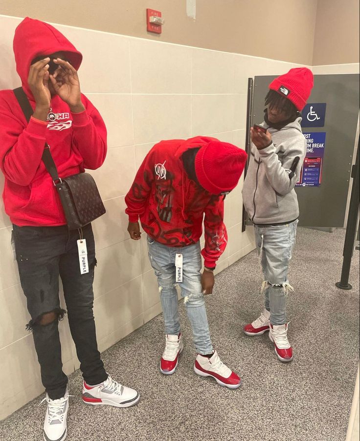 three young men in red hoodies standing next to each other and looking at their cell phones