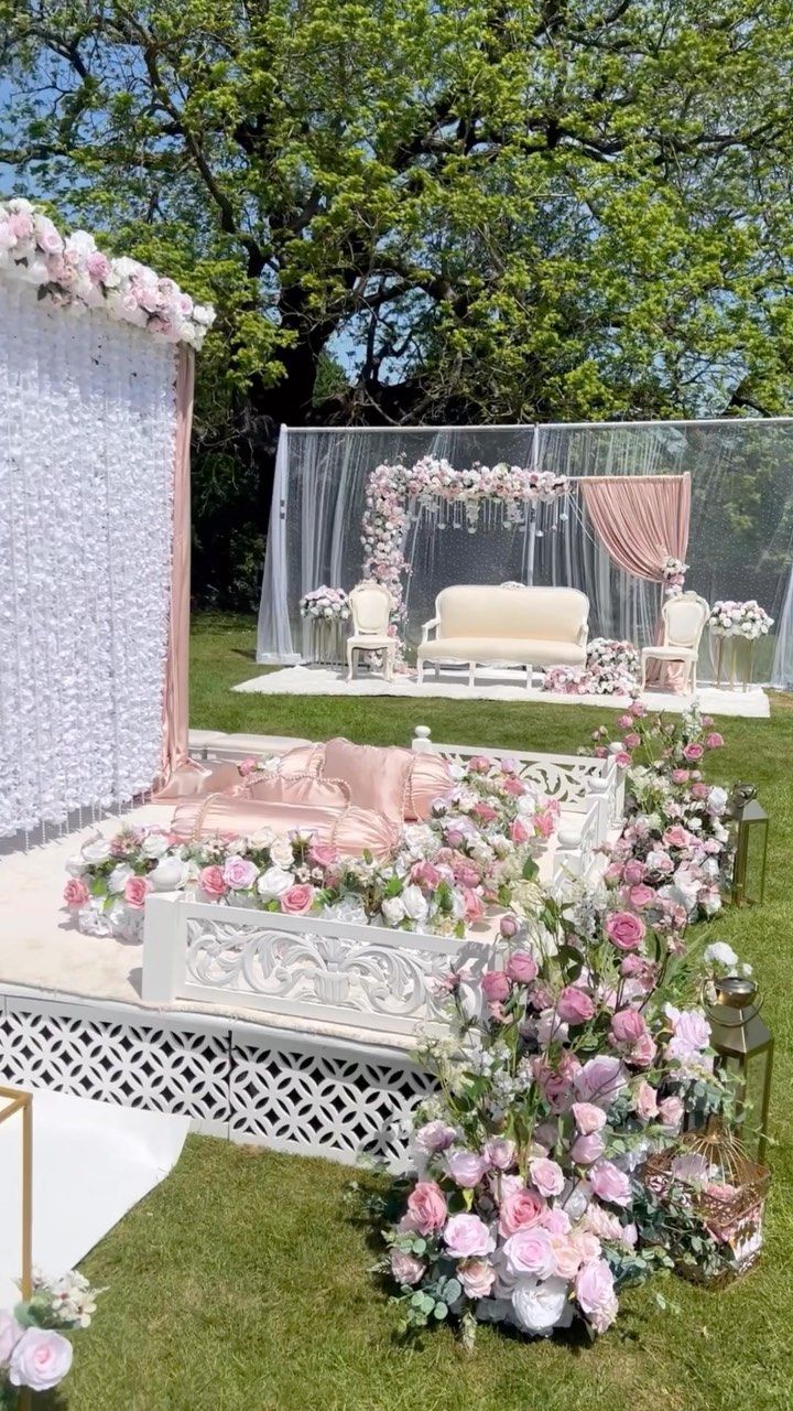 an outdoor wedding setup with pink flowers and white drapes on the side of it