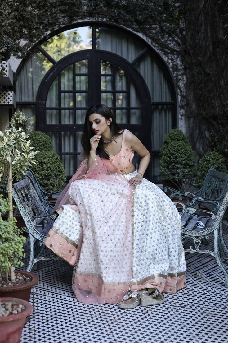 This peach and white poly paper silk lehenga has glitter flower motifs spread all over.  It is paired with an embroidered raw silk blouse and an embroidered net dupatta. White Cutdana Sharara In Tissue Silk, White Anarkali Tissue Silk Choli, White Anarkali Choli In Tissue Silk, White Tissue Silk Choli For Party, Peach Choli With Sheer Dupatta For Weddings, Peach Dupatta With Cutdana For Navratri, White Tissue Silk Choli With Pallu, White Tissue Silk Choli With Pallu Detail, White Anarkali Lehenga In Tissue Silk