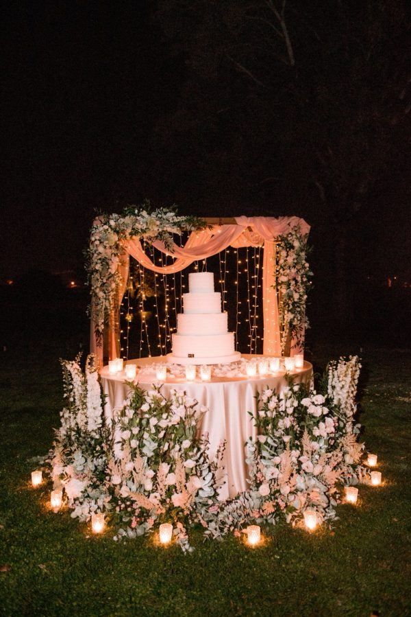 a wedding cake on a table with candles in the grass and flowers all around it