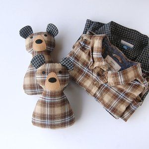 two teddy bears sitting next to each other on a white surface with plaid shirts in the background