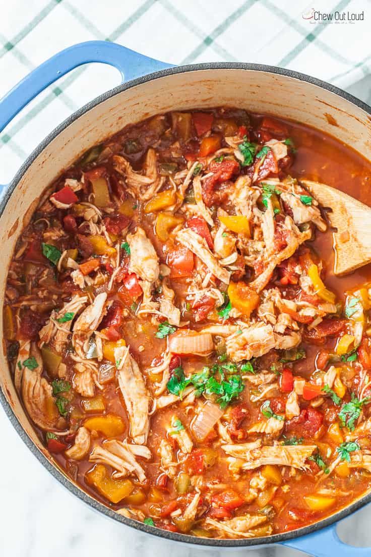 a pot full of chicken and vegetable stew with a wooden spoon in the bottom left corner