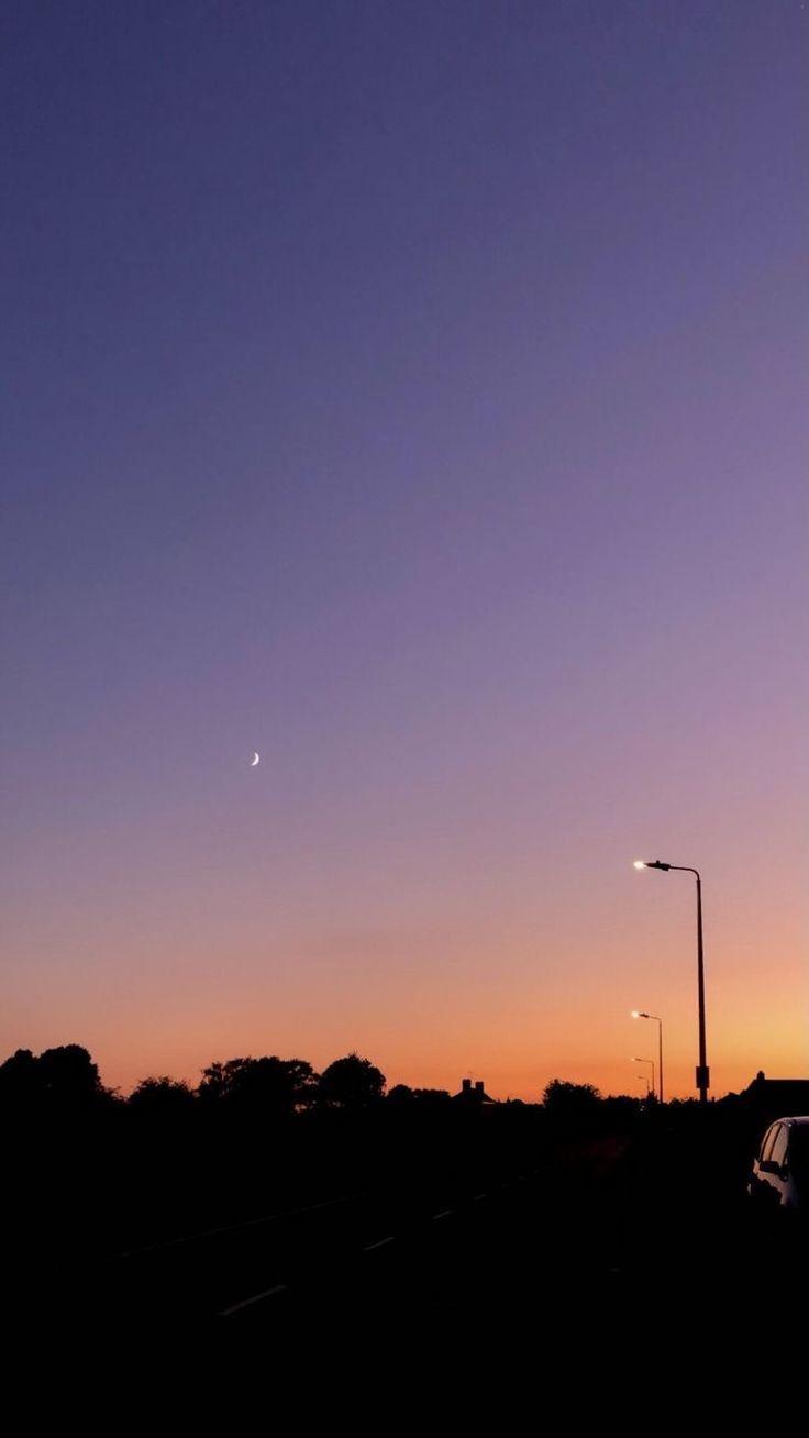 the sun is setting behind a street light