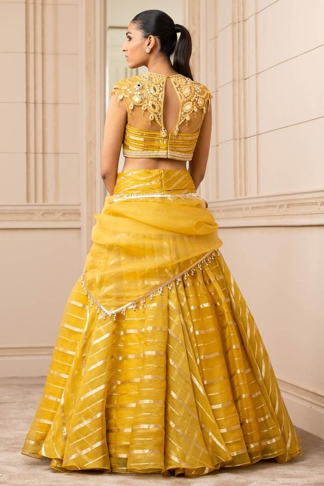 Mustard sheer brocade lehenga with a cascading drape and pearl detailing on the waistband. Paired with embroidered with resham, mirror work blouse. Comes with a matching sheer scarf embellished with fringes. Draped Lehenga, Drape Lehenga, Yellow Mirror, Brocade Lehenga, Mirror Work Blouse, Resham Work, Sheer Scarf, Blouse Back, Yellow Silk