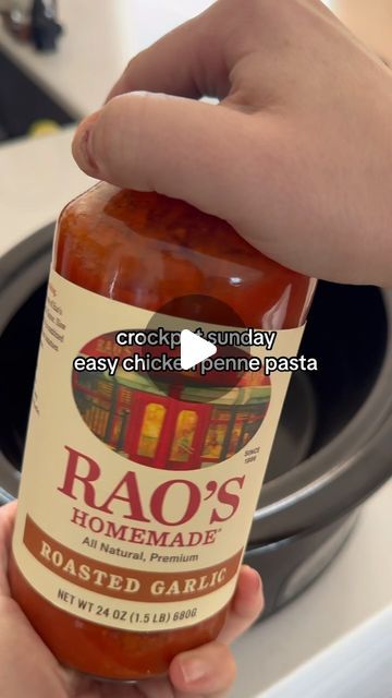 a person holding a jar of sauce in front of an open stove top oven with the words raq's homemade roasted garlic on it