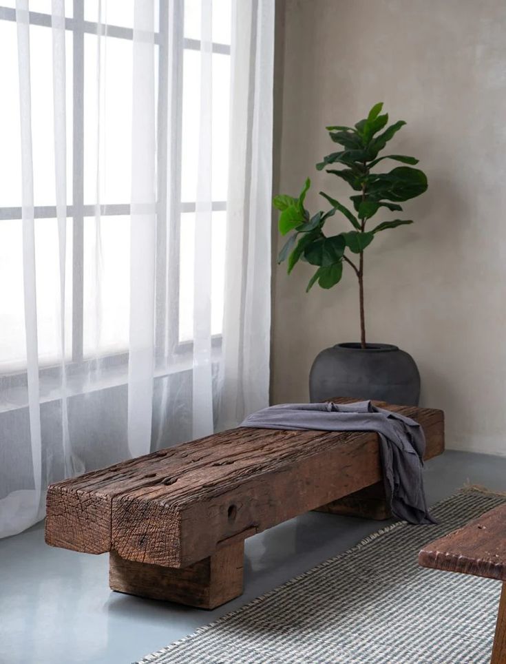 a wooden bench sitting in front of a window next to a table with a potted plant on it