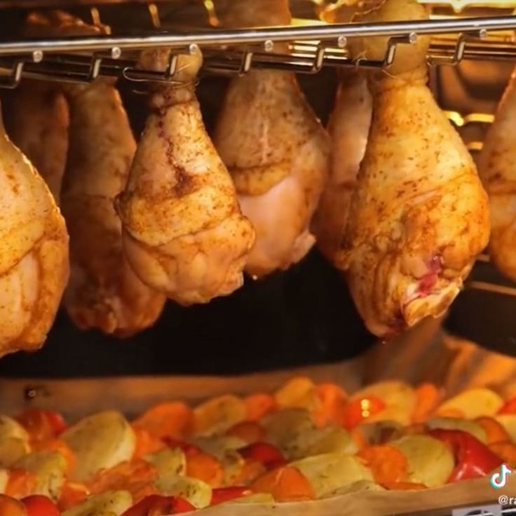 several pieces of chicken hanging from a rack in an oven with vegetables on the side