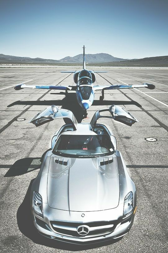 a silver sports car parked on top of an airport tarmac with two planes in the background