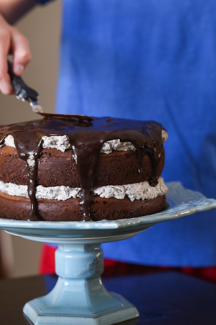 someone is cutting into a chocolate cake with white frosting on it and drizzled with chocolate