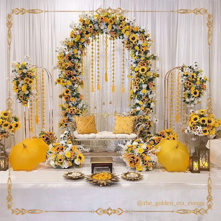 a white table topped with yellow and white flowers next to an arch covered in sunflowers