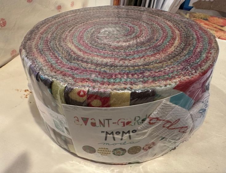 a roll of fabric sitting on top of a white table cloth covered in multicolored papers