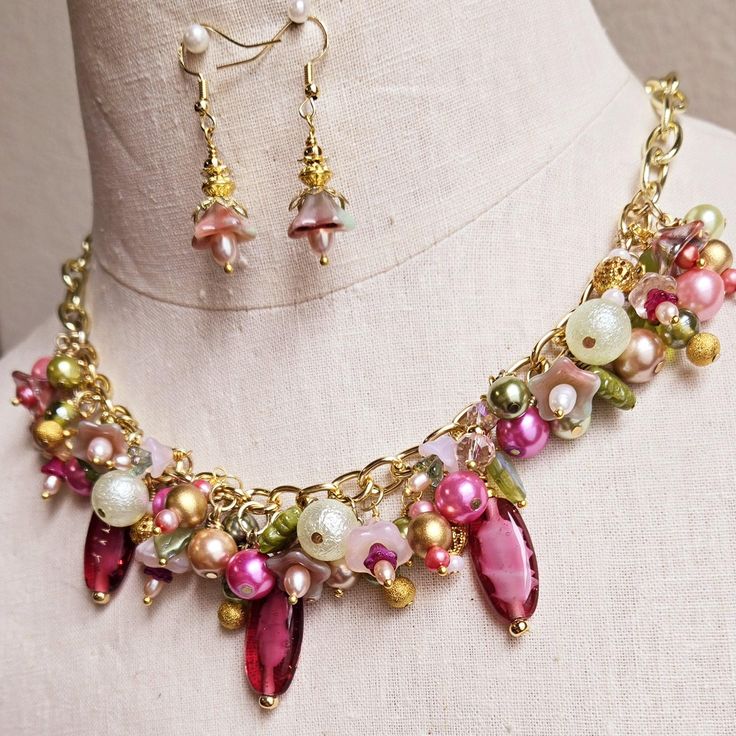 Make a statement with this one-of-a-kind floral charm necklace and earrings set. Gold wire wrapped freshwater pearls, glass pearls, cut Swarovski crystals, Czech glass flowers and leaves, gold plated findings, and assorted glass beads are hung on a gold-plated chain on the lower half of the necklace chain and finished with a matching lobster clasp.  This bright and colorful beaded necklace comes with all charms shown. Necklace length can be adjusted as requested, prior to checkout.  Matching floral earrings are hung on gold ear wires. Makes a great addition to your collection or a wonderful gift for someone special. Pink Pearl Charm Jewelry For Wedding, Whimsical Czech Glass Jewelry Set With Earrings, Whimsical Pearl Charm Jewelry For Gifts, Whimsical Pearl Charm Jewelry As Gift, Pink Pearl Dangle Necklaces, Whimsical Beaded Dangle Jewelry, Pink Pearl Charm Jewelry Gift, Pink Beaded Czech Glass Jewelry, Whimsical Dangle Jewelry With Lobster Clasp