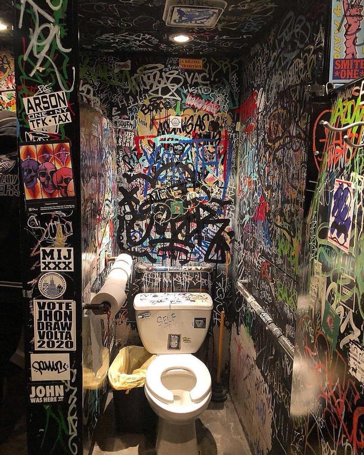 a bathroom with graffiti all over the walls and toilet in the middle of the room