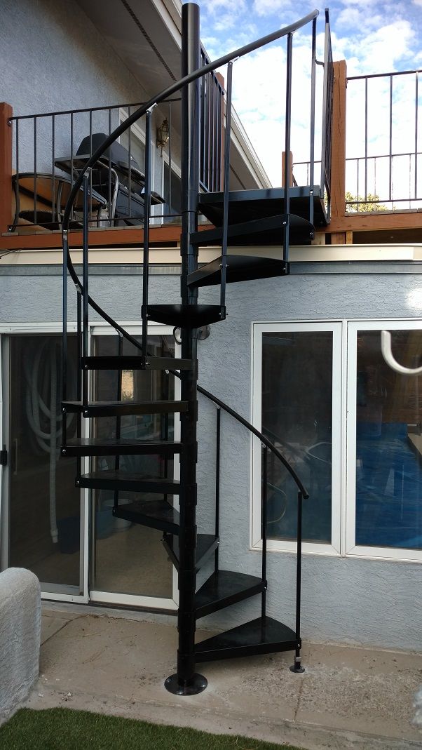 there is a black spiral staircase in front of a house with sliding glass doors on the second floor