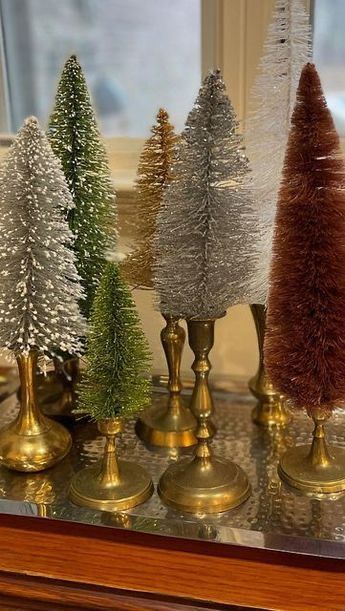 small christmas trees are lined up in gold and silver vases on a table near a window