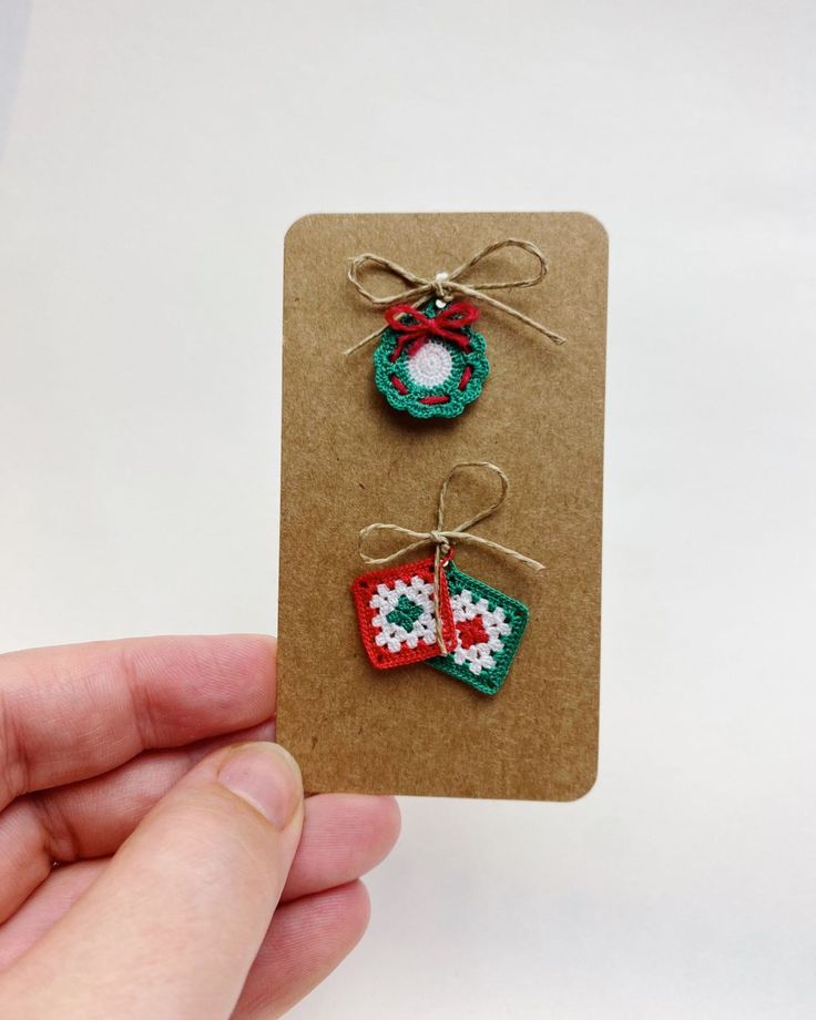 a hand holding a card with two christmas decorations on it and a tag attached to the back