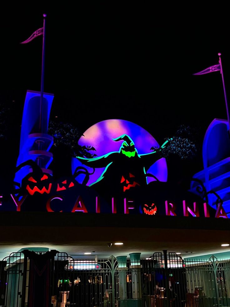 the entrance to an amusement park lit up in purple and green lights at night time