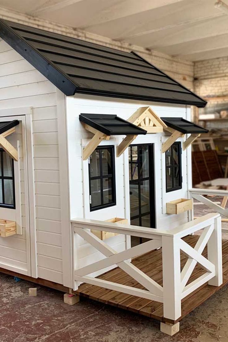 a white house with black roof and windows on top of a wooden platform in a warehouse