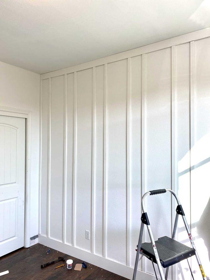 an empty room with white paneling on the walls and a ladder next to it