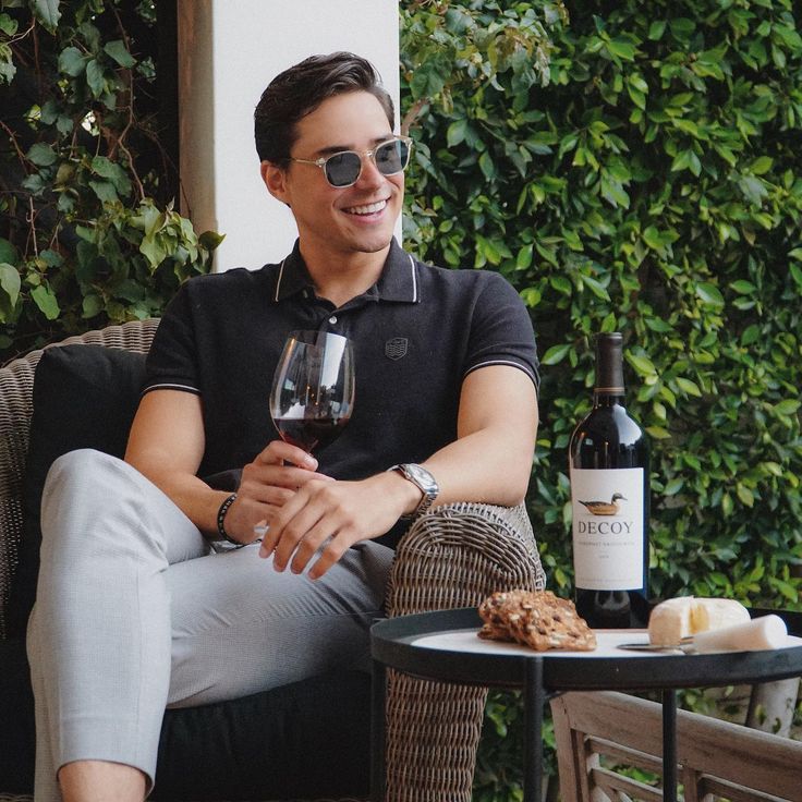 a man sitting on a chair with a glass of wine in his hand next to a bottle of wine