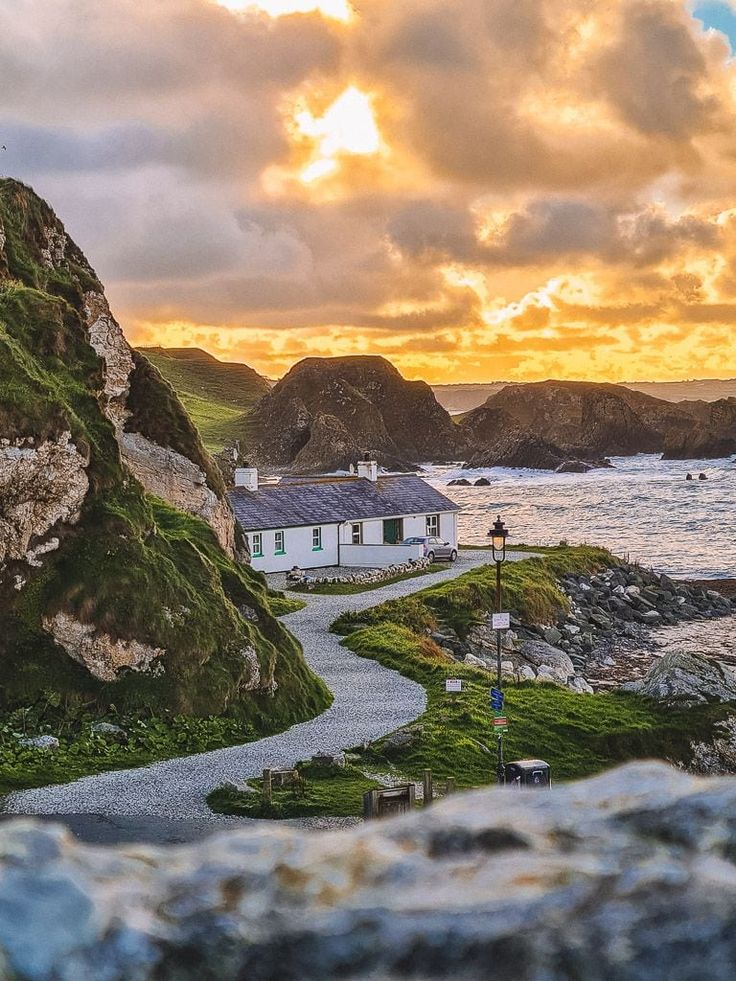 a white house sitting on top of a lush green hillside next to the ocean under a cloudy sky