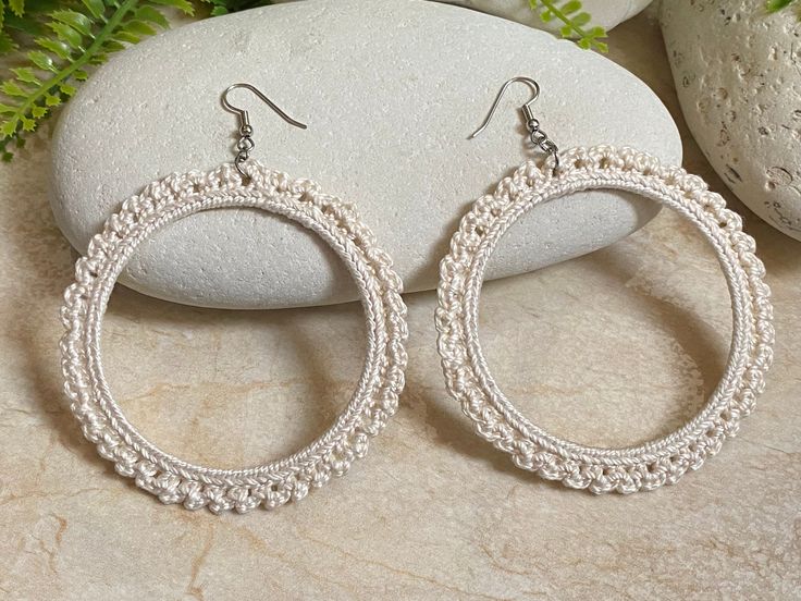 a pair of white beaded hoop earrings sitting on top of a rock next to some plants