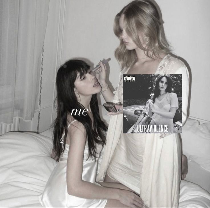 two women sitting on a bed one holding a magazine and the other looking at her