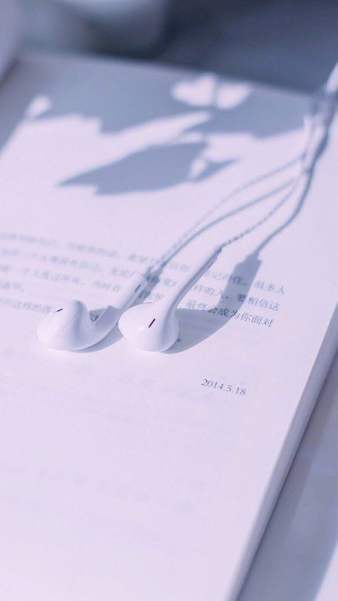 two white earbuds laying on top of an open book with the shadow of a person's head