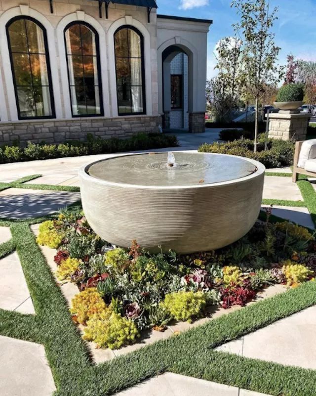 an outdoor fountain surrounded by grass and flowers