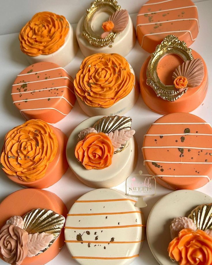 there are many decorated cookies on the table with orange frosting and gold trimmings