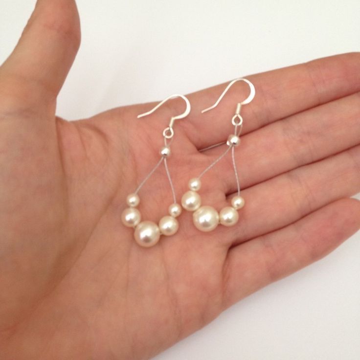 a hand holding some white pearls on it's fingers and wearing silver earwires