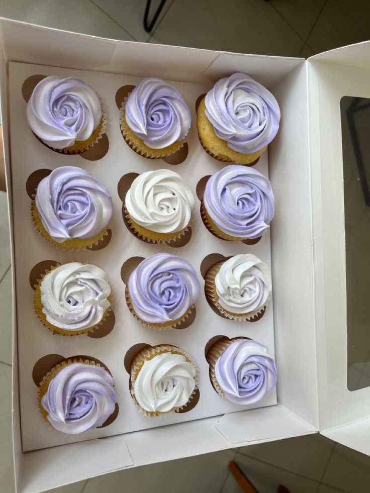 twelve cupcakes in a white box with purple frosting on the top and bottom